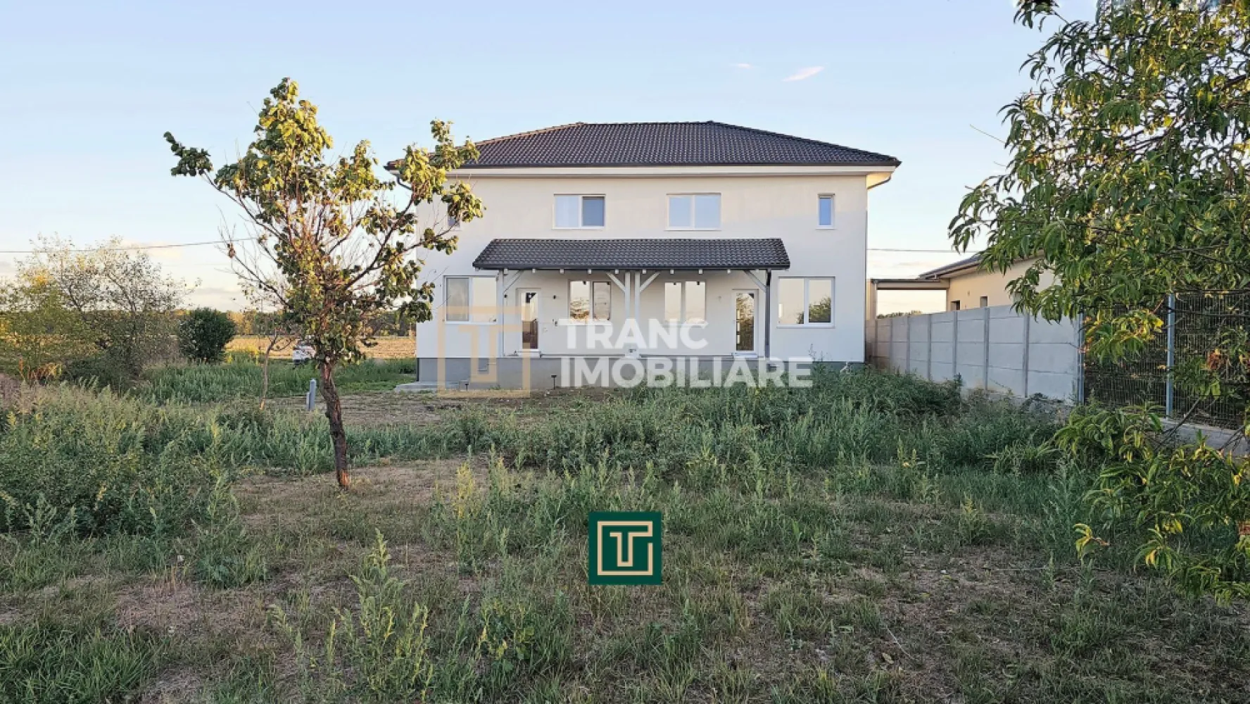 Jumătate de duplex nou cu 4 camere in Vladimirescu - În Vladimirescu, într-o zonă liniștită, dar cu acces rapid la centura Aradului, Tranc Imobiliare vă oferă la vânzare o locuinta formata din jumatate dintr-un duplex nou, finalizat în 2025 și pregătit să fie locuit imediat. Locuința se predă la cheie, nemobilată, cu finisaje moderne și de calitate superioara, gândite pentru a oferi un ambient elegant și ușor de personalizat de către viitorii proprietari.

Suprafața construită este de 154 mp, iar cea utilă de 96 mp, desfășurată pe parter, mansardă și pod. Terenul are 342 mp, cu un front stradal de 8 metri și acces direct din drum asfaltat. Compartimentarea este practică și bine gândită: living luminos, bucătărie spațioasă, trei dormitoare, două băi complet funcționale, o terasă acoperită de 7,6 mp, dar și o cameră tehnică situată sub scară, unde se află centrala termică și spațiu suplimentar pentru depozitare și mașina de spălat. În fața casei, proprietarii beneficiază de o parcare acoperită de 18 mp.
Finisajele interioare sunt moderne și luminoase, cu pardoseli din parchet și gresie în tonuri calde, pereți zugrăviți cu lavabil alb, plinte elegante, uși interioare albe cu design contemporan și băi complet amenajate cu faianță de bun gust. Totul este nou și pregătit pentru a fi folosit din prima zi.

Din punct de vedere tehnic, casa este solid construită, cu pereți din cărămidă, fundație de beton și acoperiș din țiglă ceramică. Izolația exterioară din polistiren de 10 cm asigură eficiență energetică, iar instalațiile electrice din cupru și cele sanitare din PPR oferă durabilitate. Încălzirea se realizează prin centrală pe gaz, cu incălzire în pardoseală. Proprietatea este racordată la toate utilitățile, apă, gaz, curent trifazic, canalizare.
Chiar dacă dormitoarele sunt mai compacte, avantajele acestei proprietăți, prin faptul că este o construcția nouă, finisajele sunt moderne, are eficiența energetică ridicată și zona este liniștită, dar totuși aproape de centură si de zona centrală a satului Vladimirescu, o transformă într-o alegere foarte bună atât pentru locuință permanentă, cât și ca investiție.

Curtea poate fi transformată într-o grădină verde, cu gazon, flori și arbori, sau într-un spațiu de relaxare cu foișor și loc de grătar. Pentru familiile cu copii, terenul poate deveni loc de joacă privat, iar pentru cei care apreciază confortul, există suficient spațiu pentru o piscină mică ori o zonă de terasă extinsă. Astfel, cumpărătorul nu achiziționează doar o locuință modernă, ci și libertatea de a-și crea propriul colț de liniște și confort după dorințe.

Această locuința este soluția ideală pentru o familie care își dorește o casă nouă, bine compartimentată și gata de locuit, unde tot ce rămâne de făcut este să fie mobilată și decorată după gustul personal.