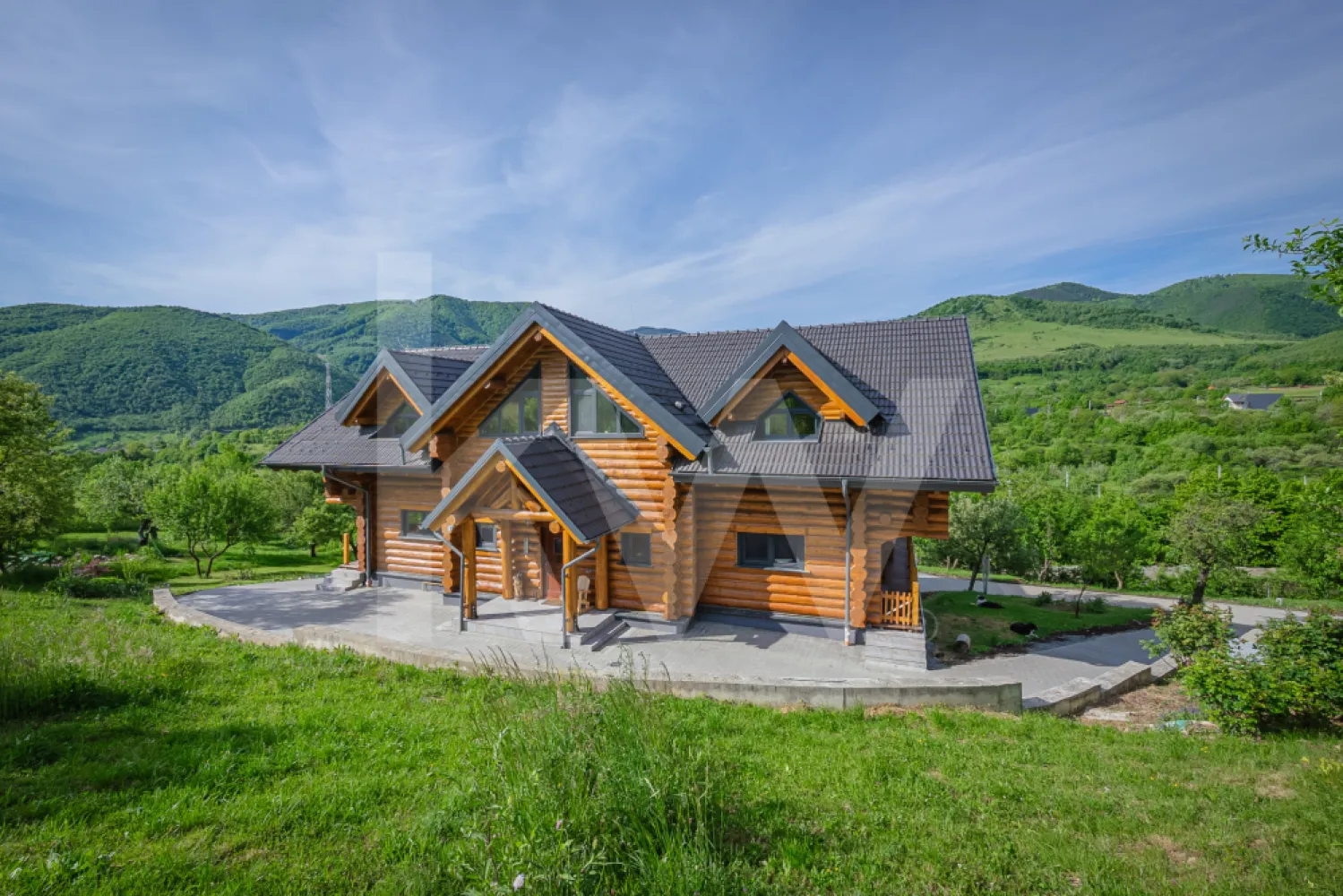 Mai mult decât spațiu: timp, liniște și confort în natură. - Unele proprietăți se cumpără pentru numărul de metri pătrați. Altele… pentru felul în care te lasă să respiri.

Știm cum e. Te trezești în zgomotul orașului, alergi între ecrane, betoane și termene limită, iar uneori simți doar nevoia să te oprești. Să respiri aer curat. Să vezi cerul liber, fără un alt bloc care să-ți taie orizontul.

Această casă nu este doar o proprietate de vânzare; este un loc care a fost creat exact ca un răspuns la această oboseală. Este un refugiu din bușteni masivi de 40 cm, aduși din păduri europene certificate (unde fiecare copac tăiat înseamnă respect pentru natură și mediu). Cei care au construit-o au fost acolo, zi de zi, punând suflet în fiecare grindă. De aceea, când pășești înăuntru, simți o căldură pe care nicio clădire modernă de sticlă nu ți-o poate oferi. Lemnul miroase a tihnă, iar timpul pare că decide, în sfârșit, să încetinească.

Aici, viața se așază altfel, pe trei niveluri gândite cu grijă și blândețe:
Demisolul (136 mp) – Spațiul pentru tine și pasiunile tale 
Ascuns parțial de ochii lumii, acest nivel este locul tău de relaxare și utilitate. Pe lângă garajul dublu cu uși electrice, camera tehnică, baia cu duș (showerroom) și spațiile de depozitare foarte generoase, vei descoperi o zonă de lounge, o cămară și un atelier/birou. Imaginează-ți cum e să deschizi ușa acestui atelier direct spre curte, în timp ce lucrezi la un proiect de suflet sau pur și simplu te bucuri de un moment de liniște, doar tu cu gândurile tale.

Parterul (138 mp) – Locul unde familia se adună la căldură 
Inima casei este un living grandios (Great Room) de aproximativ 50 mp, cu tavan boltit care pune în valoare structura spectaculoasă din bușteni și un balcon interior (galleried landing). Spațiul este centrat în jurul unui șemineu superb și inundat de lumină naturală. Tot aici ai un hol generos de la intrare, toaletă și garderobă, două camere interconectate de câte 17 mp și o bucătărie spectaculoasă de 37 mp. Din bucătărie ieși direct pe terasa de 70 mp – locul perfect unde diminețile încep cu o cafea băută fără grabă și aer curat în piept.

Etajul – Refugiul tău sub cerul liber 
Sus, liniștea devine și mai profundă. Te așteaptă un hol impresionant de la etaj, de tip balcon interior, de aproximativ 30 mp, cu o zonă suplimentară de birou de 9 mp. Cele două dormitoare spațioase de aproximativ 17 mp fiecare și dormitorul matrimonial generos de 28 mp au un detaliu special: fiecare are propriul balcon privat cu vederi spectaculoase spre munții din jur. Să deschizi ușa dimineața, direct din pat, este un ritual care vindecă orice zi grea. Etajul este completat de o baie pentru oaspeți de 10 mp, precum și o baie en-suite de 8 mp pentru dormitorul matrimonial, dotată cu o cabină de duș dublă și paravan de sticlă (rain shower).

O casă care are grijă de tine (Sustenabilitate și independență): 
-Adevărata grijă înseamnă și siguranță. Casa este complet conectată la rețelele de utilități (apă, canalizare, energie electrică), dar îți oferă o independență totală și blândă cu planeta: 
-Încălzirea în pardoseală (la parter și etaj) și caloriferele (la demisol) îți oferă o căldură uniformă. 
-Sistemul fotovoltaic de 12.5 kW cu baterii de stocare și circuit bidirecțional produce energie curată. 
-Boilerul masiv de 1500 L cu sistem de filtrare și rezervorul de gaz de 1000 L îți asigură tot confortul. 
-Iar bazinul de urgență de 7000 L este acolo ca o plasă de siguranță pentru udatul grădinii sau momente neprevăzute.

Cu un teren total de 5.683 mp, ai la dispoziție o zonă verde liberă de 5.003 mp (plus 620 mp de curte pavată). Este propriul tău parc. O mică oază cu apă care curge liniștit, o grădină de legume unde poți redescoperi gustul roșiilor proaspete culese cu mâna ta și o intimitate totală. Nimeni nu te grăbește, nimeni nu te privește.

Și poate cel mai cald colț: Pub-ul privat de 20 mp. Un loc doar al tău și al prietenilor tăi vechi, unde depănați amintiri, ascultați muzică bună la un pahar de vin și uitați complet de telefoane.

Ești la doar câteva minute distanță de oraș, dar destul de departe pentru a putea auzi, în sfârșit, liniștea.
Aceasta nu este doar o casă de cumpărat. Este locul în care înveți din nou să trăiești în tihnă. Să asculți ploaia căzând pe lemnul cald. Să privești apusul și să simți că ești, în sfârșit, acasă.
Dacă simți că acesta este ritmul pe care îl cauți, te așteptăm să o simți și la fața locului.