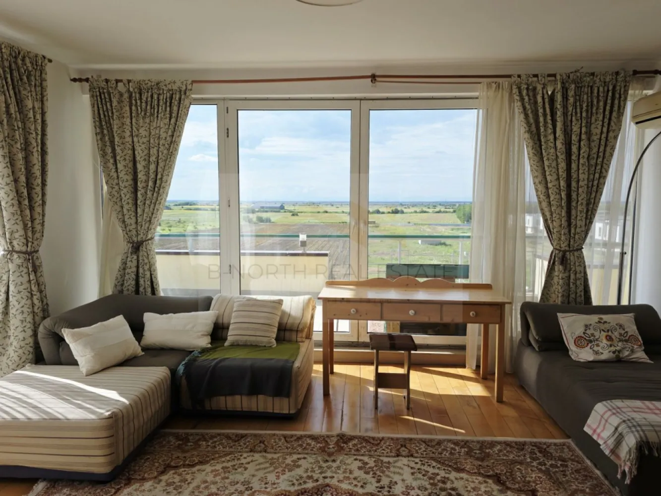 Penthouse 148mp cu terase75 mp și șemineu | Corbeanca - B-North Real Estate vă prezintă spre inchiriere, un penthouse cu suflet, view panoramic și terase generoase, situat în complexul rezidențial North Point Corbeanca, în Ostratu – un loc în care liniștea, natura și confortul se îmbină perfect cu accesul rapid către nordul Bucureștiului.
Sunt locuințe care se aleg pentru suprafață.
Și sunt locuințe care se simt din primul moment.
Acest penthouse face parte din a doua categorie: o locuință luminoasă, aerisită, cu spații generoase, șemineu, terase ample și o priveliște superbă, deschisă către natură. Este genul de apartament în care simți libertatea unei case, dar păstrezi confortul unui complex rezidențial închis.
Proprietatea este situată la etajul 4 al unui imobil cu lift și oferă o atmosferă rar întâlnită într-un apartament: multă lumină naturală, intimitate, vedere panoramică și zone de relaxare atât la interior, cât și la exterior.
Locuința dispune de aproximativ 148 mp interiori, completați de aproximativ 75 mp de terase, perfecte pentru cafeaua de dimineață, seri liniștite, plante, zonă de lounge sau mese în aer liber cu vedere deschisă.
Zona de zi este unul dintre cele mai frumoase puncte ale proprietății: living amplu, dining luminos, șemineu și acces către terase. Este un spațiu cald și primitor, potrivit pentru familie, seri cu prietenii sau momente de liniște acasă, departe de agitația orașului.
Se vinde mobilat și utilat, cu electrocasnice incluse, oferind o bază foarte bună pentru o locuință spectaculoasă, care poate fi ușor personalizată de viitorul proprietar.
Compartimentarea include:
living generos cu acces către terasă
zonă de dining cu vedere panoramică
bucătărie separată, mobilată și utilată
2 dormitoare,2 băi,spații de depozitare,șemineu,terase ample, cu priveliște deschisă,loc de parcare inclus
Complexul North Point Corbeanca este un complex rezidențial închis, cu acces securizat cu barieră, loc de joacă pentru copii, spații verzi și o frumoasă alee de platani la intrare. Atmosfera este una elegantă, aerisită și relaxată – ideală pentru familii, pentru persoane care lucrează de acasă sau pentru cei care își doresc să locuiască aproape de natură, dar nu izolați.
Poziționarea este un avantaj important. Deși te bucuri de liniște, aer curat și intimitate, ai acces rapid către punctele importante din nordul Capitalei:
aproximativ 10-15 minute până la Aeroportul Otopeni
aproximativ 10-15 minute până la Therme București
aproximativ 15-20 minute până la Băneasa Shopping City și zona comercială Băneasa
aproximativ 25-35 minute până în nordul Bucureștiului, în funcție de trafic
În apropiere se regăsesc supermarketuri, restaurante, grădinițe, școli, centre comerciale și zone de relaxare, păstrând în același timp sentimentul de retragere într-o zonă verde și liniștită.
Acest penthouse este o alegere excelentă pentru cei care caută mai mult decât un apartament: caută spațiu, lumină, terase, view, siguranță și o atmosferă de acasă.